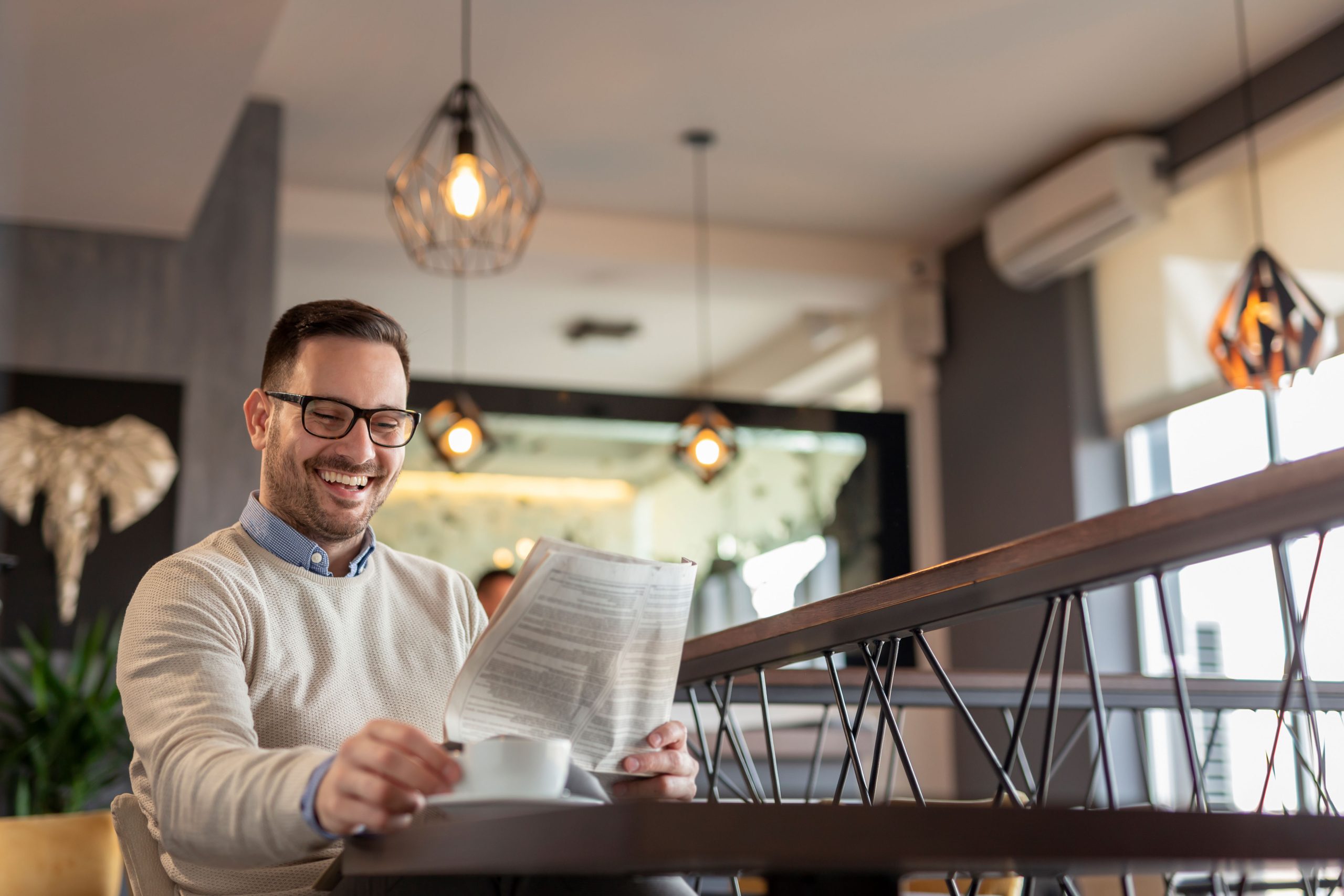 Man,Sitting,At,A,Restaurant,Table,,Reading,Newspaper,And,Drinking